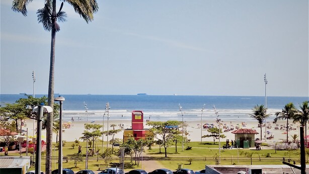 Blick auf einen Strand mit Palmen, einem roten Gebäude und geparkten Autos.