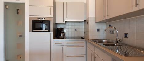 A modern kitchen with white cabinets, a built-in oven, a coffee maker, and a stainless steel sink.
