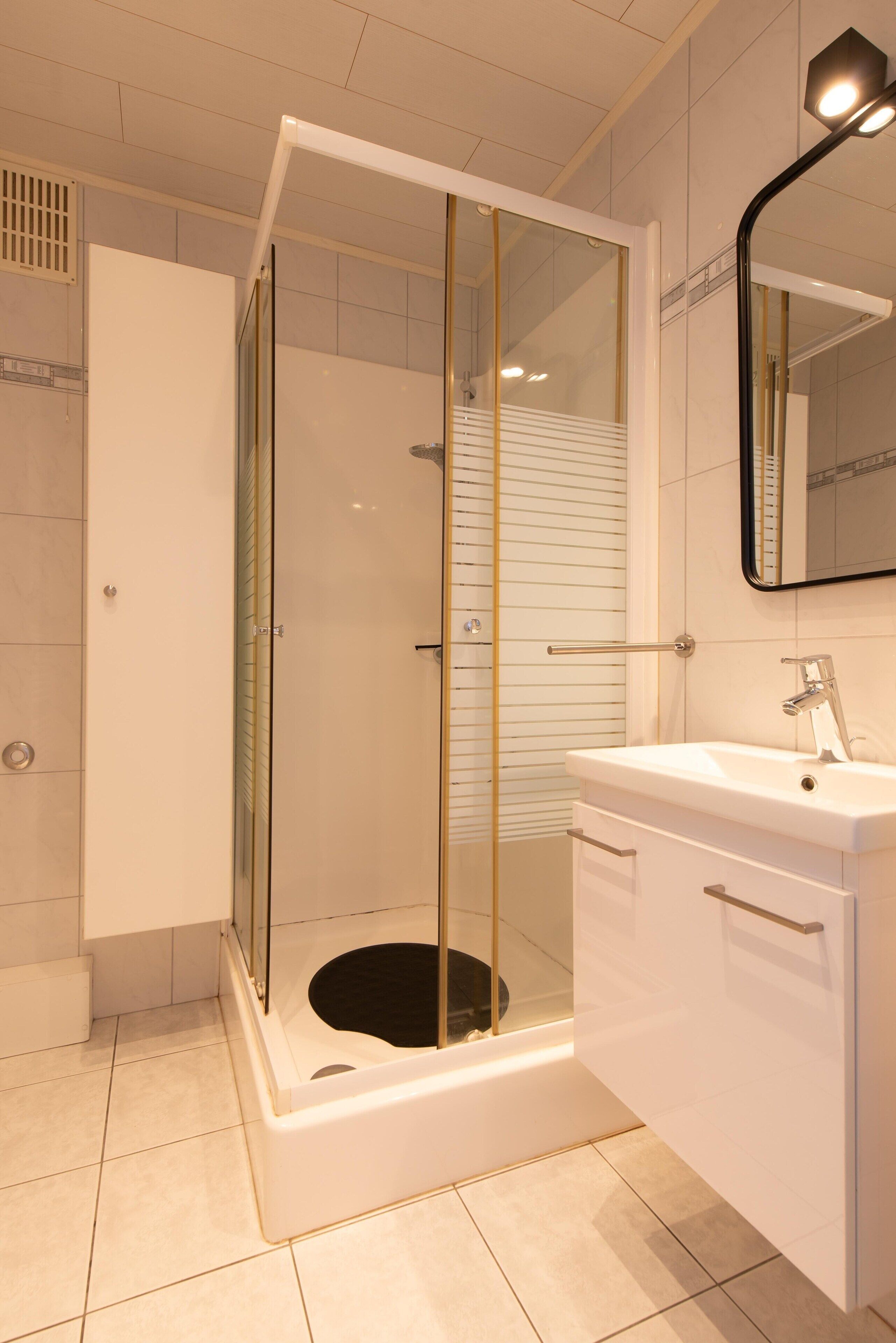 Une salle de bain moderne avec une douche à parois de verre, un lavabo blanc et un miroir.