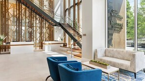 A modern hotel lobby with a reception desk, blue chairs, a staircase, and a large window with a view of greenery. - Wyndham Vacation Resort Downtown ATL walking distance to MercedesBenz Stadium (Atlanta)