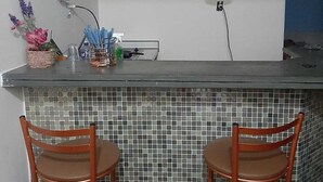 Una cucina con angolo bar, due sedie di legno, zoccolo a mosaico e tre lampade a sospensione in rame.