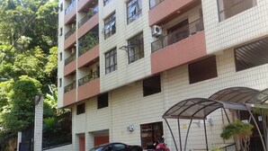 Un edificio a più piani con facciata in tegole, balconi e un’area d’ingresso coperta con piante in vaso.
