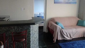 Una stanza con un letto, una sedia, un tavolino, un quadro e vista mare attraverso una porta aperta.