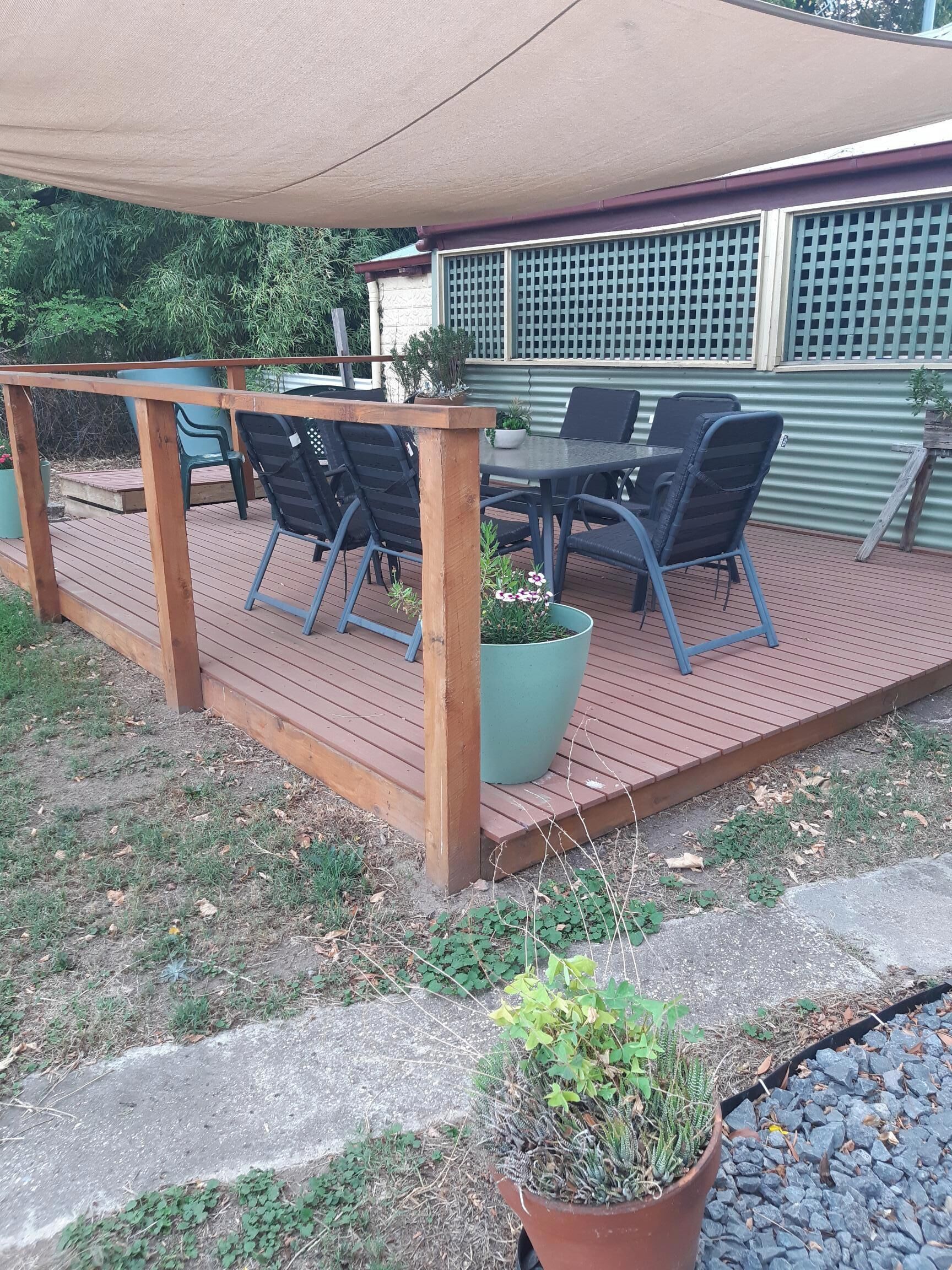 Eine Holzterrasse mit Gartenmöbeln, darunter Stühle und ein Tisch, in schattigem Bereich.