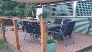 En træterrasse med udendørs møbler, herunder stole og et bord, under et skyggefuldt område.