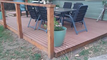 Eine Holzterrasse mit Gartenmöbeln, darunter Stühle und ein Tisch, in schattigem Bereich.