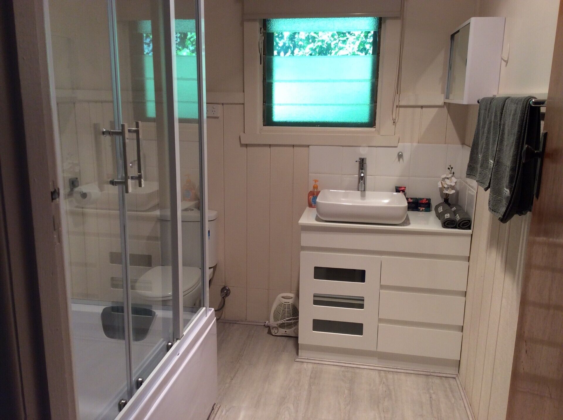 Un baño con ducha envuelta en vidrio, lavabo con ventana superior y barra para toallas.