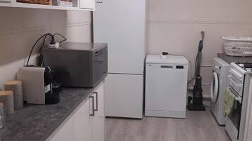 Cocina compacta con muebles blancos, lavadora integrada, refrigerador y cafetera.