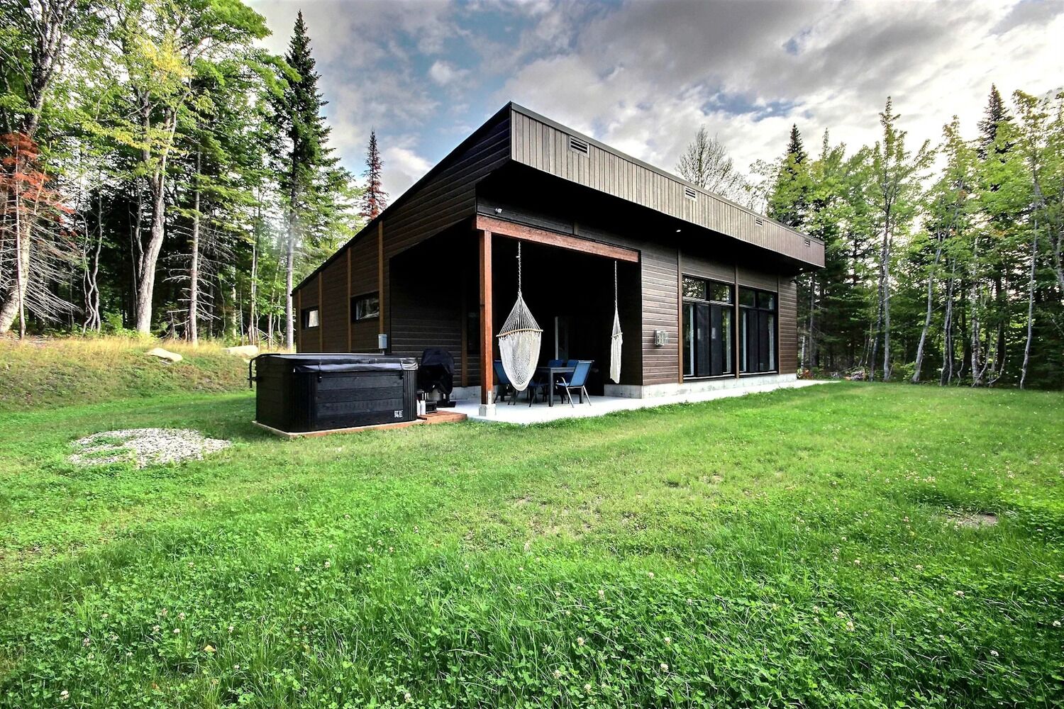 A modern cabin with a covered patio, a hot tub, and a hammock.