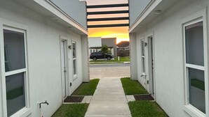 Un sendero que lleva a un edificio con vistas al atardecer, rodeado de edificios blancos y un coche estacionado.