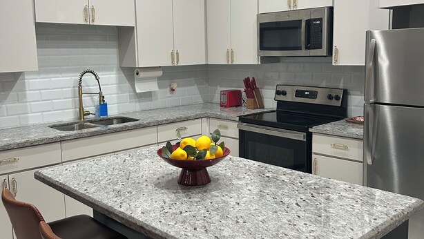 Una cocina moderna con armarios blancos, encimera de granito, microondas integrado, refrigerador de acero inoxidable y un cuenco de limones en la isla.