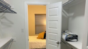 Una habitación pequeña y bien iluminada, con una cama, un armario y una puerta que da a otra habitación.