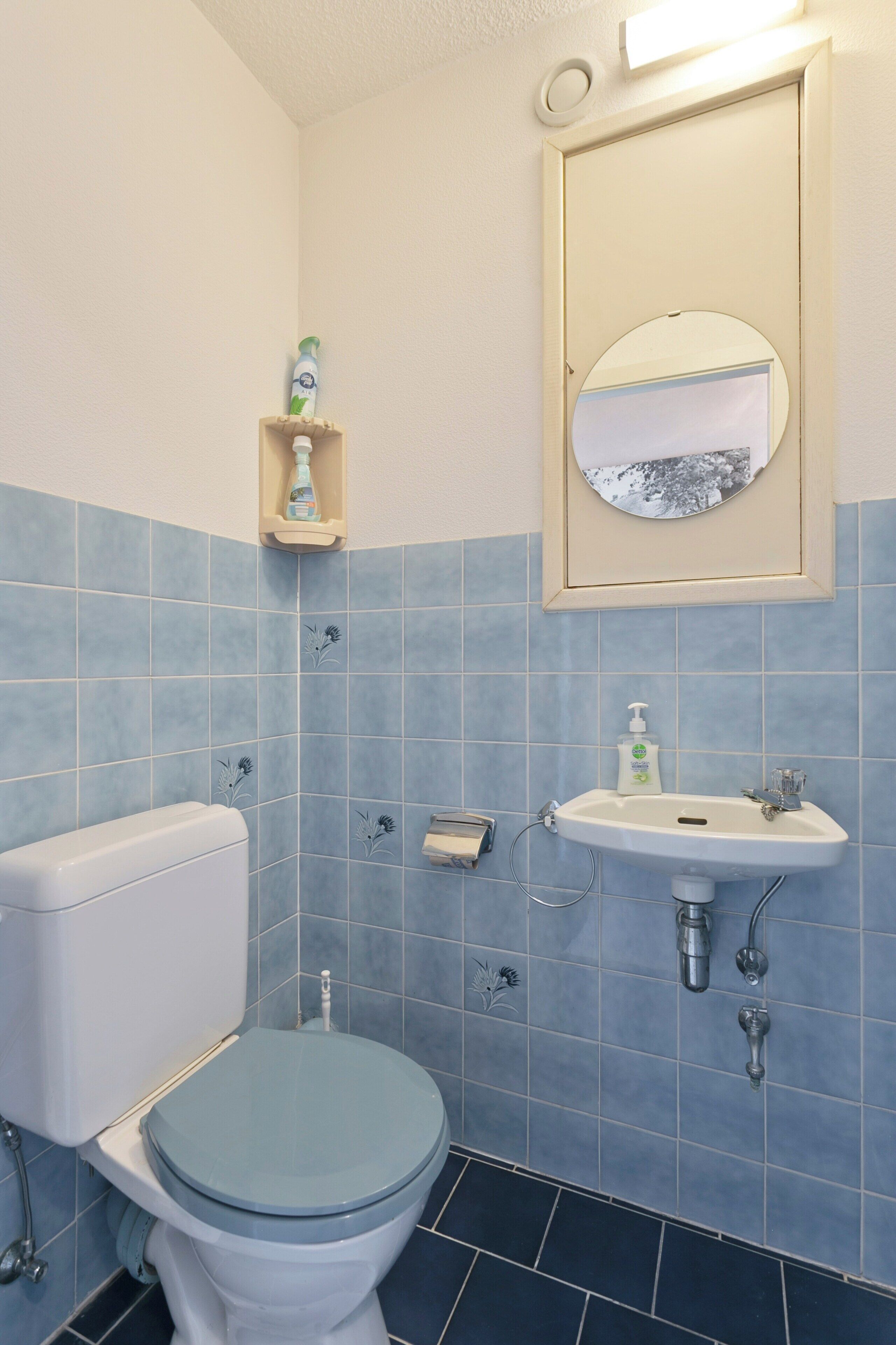 A bathroom with a toilet, sink, and mirror.