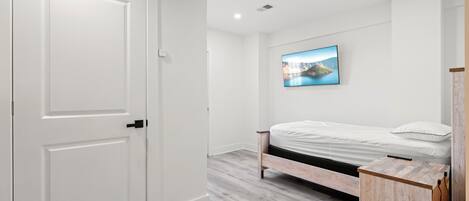 A bedroom with a bed, a white door, a wooden cabinet, and a wall-mounted TV.