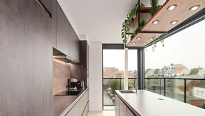 A modern kitchen with dark wood cabinets, a stainless steel countertop, and a window overlooking a cityscape. - Apartment in Blankenberge Near the Beach (Blankenberge)