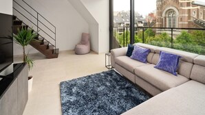 A modern living room with a large window, a staircase, a bean bag, a sofa with cushions, and a TV on a cabinet. - Apartment in Blankenberge Near the Beach (Blankenberge)