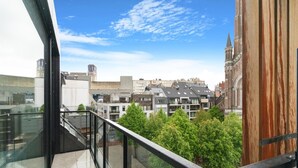 A balcony with a glass railing overlooking a cityscape with modern buildings and a church tower. - Apartment in Blankenberge Near the Beach (Blankenberge)