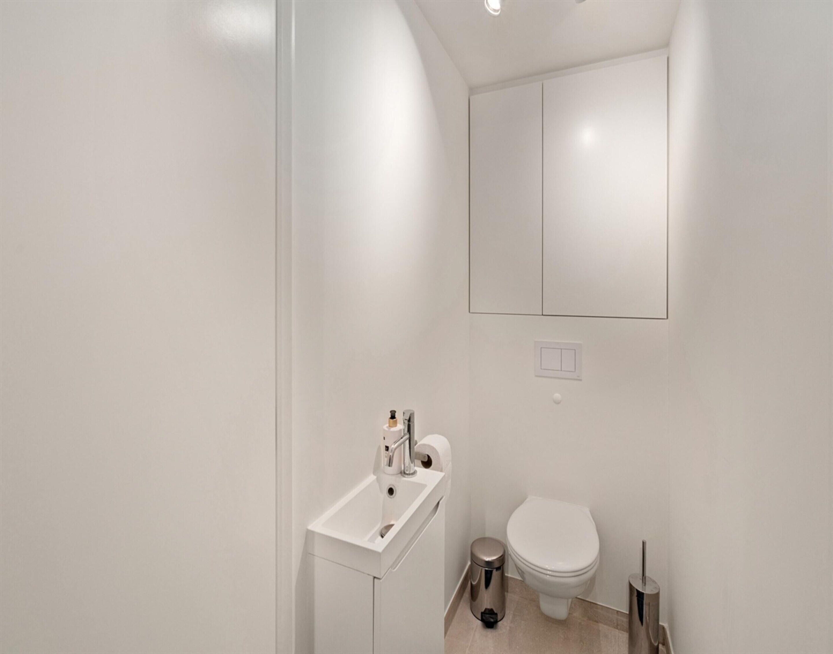 A modern bathroom with a white sink, toilet, and a mirror above the sink.