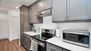 A modern kitchen with grey cabinets, a stainless steel oven, a microwave, and a white countertop. - Serenity Studios: Near Medical Center & Museum District (Houston)