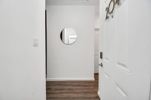 Un couloir avec une porte blanche, un miroir rond accroché au mur et un plancher en bois.