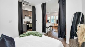 A modern hotel room with a large bed, a kitchenette, and a view of the living area. - Serenity Studios: Near Medical Center & Museum District (Houston)