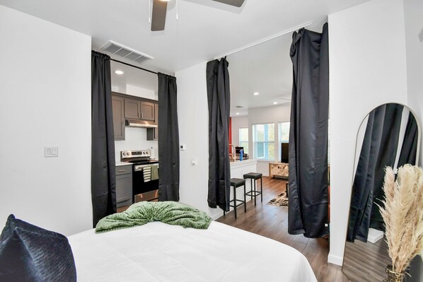 Habitación de hotel moderna con una cama grande, una kitchenette y vistas al área de estar.