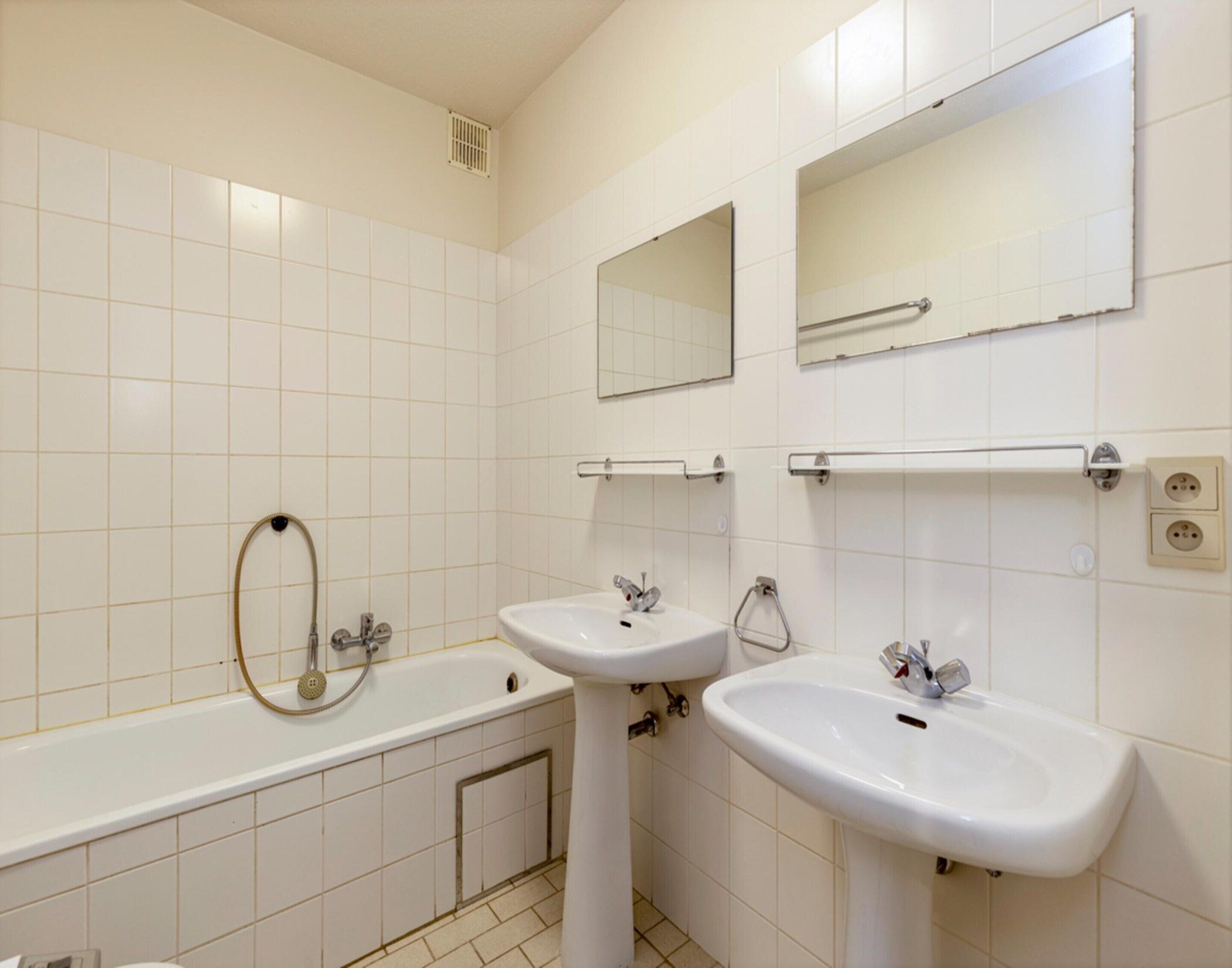 Een badkamer met twee wasbakken, een badkuip en twee spiegels.