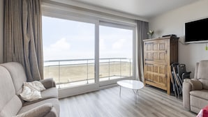 Un ampio soggiorno con una grande finestra vista mare, un mobiletto in legno, un tavolino da caffè bianco e un divano.