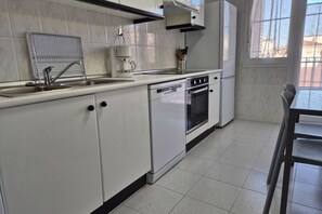 Une cuisine avec des meubles blancs, un évier, une machine à café et une fenêtre.