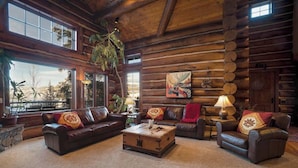 A log cabin interior with a large window, leather sofas, a wooden coffee table, and a painting on the wall.