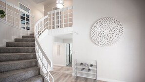 A staircase with a white railing, a wall-mounted decorative piece, and a shoe rack. - Vegas Luxe- 6BR & 3 BT pool/spa/bbq/golf<10min to Strip, Airport, Stadium & More (Las Vegas)