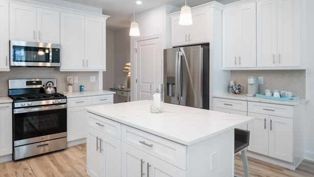 Une cuisine moderne avec des meubles blancs, des appareils en acier inoxydable et des luminaires suspendus.