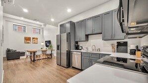 A modern kitchen with grey cabinets, stainless steel appliances, and a dining area with a wooden table and chairs. - 3Bd+65"TV+Crib+8 Min from DT CLE (Cleveland)