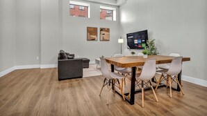 A modern living room with a wooden dining table, grey sofa, and a flat-screen TV mounted on the wall. - 3Bd+65"TV+Crib+8 Min from DT CLE (Cleveland)