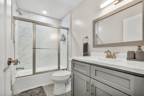 A modern bathroom with a glass-enclosed shower, a white toilet, and a vanity with a mirror and sink. - 3Bd+65"TV+Crib+8 Min from DT CLE (Cleveland)