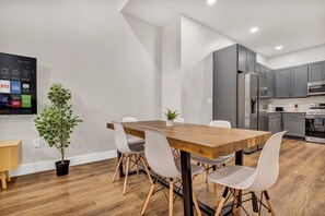 A modern kitchen with grey cabinets, a wooden dining table, and a potted plant. - 3Bd+65"TV+Crib+8 Min from DT CLE (Cleveland)