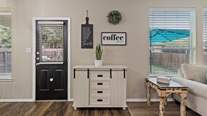 Una sala de estar con una puerta negra, un armario blanco con cajones, un letrero de café y una mesita.