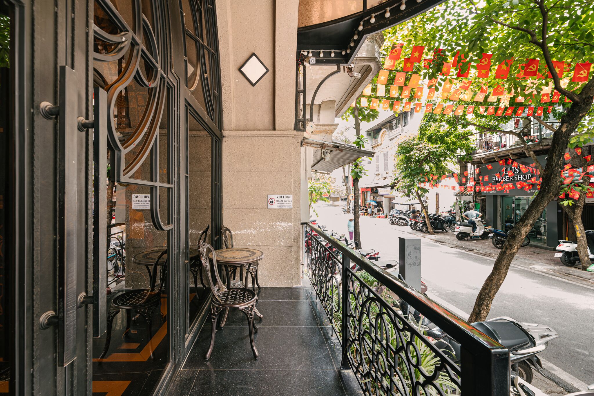 A balcony with a view of a street, a sign for a barber shop, and a tree with hanging decorations.