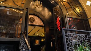 Entrada de hotel con un arco curvo, una araña y un letrero sobre la puerta.