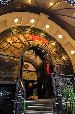 A hotel entrance with a curved archway, a chandelier, and a sign above the door. - Bay Luxury Beijing Hotel (Hanoi)