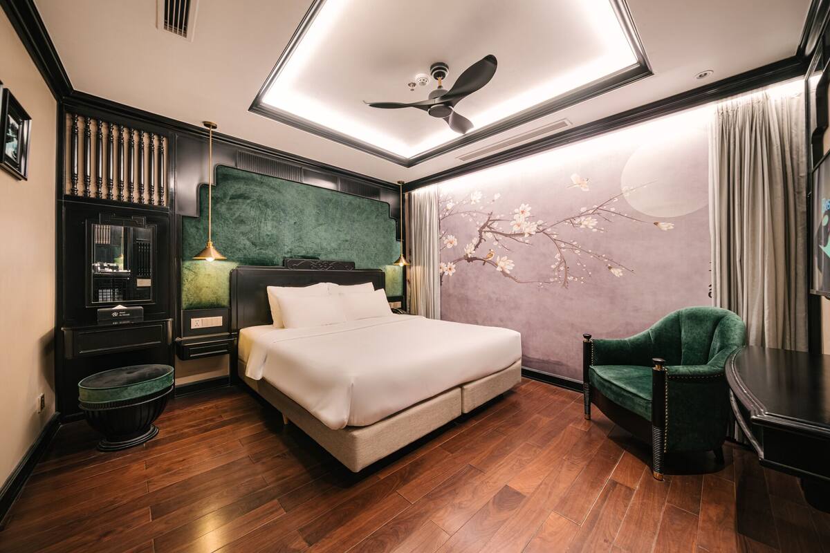 Ein modernes Hotelzimmer mit einem großen Bett, einem grünen Sessel, einem Schreibtisch und einer Wandverzierung mit einem Ast.