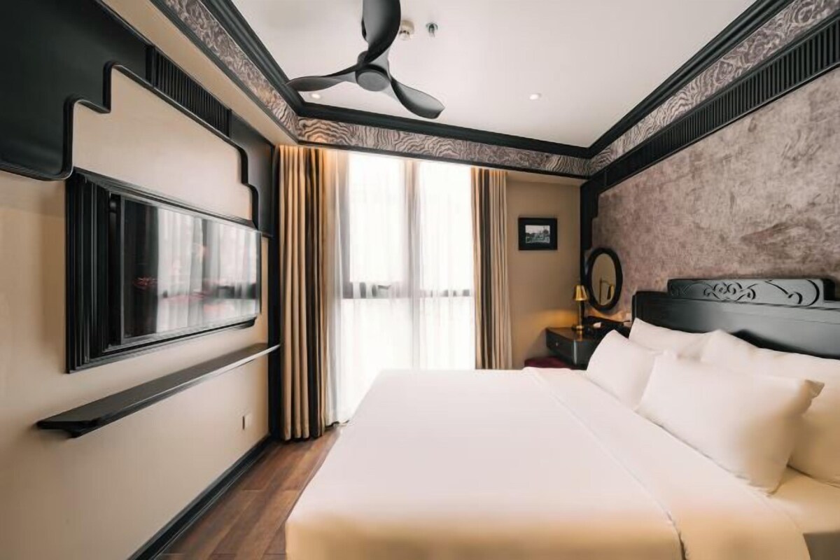A hotel room with a large bed, a ceiling fan, a TV, and a view of the outdoors.