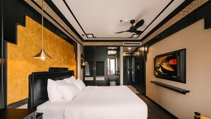 Una habitación de hotel moderna con una cama grande, un ventilador de techo, un televisor montado y un escritorio pequeño.