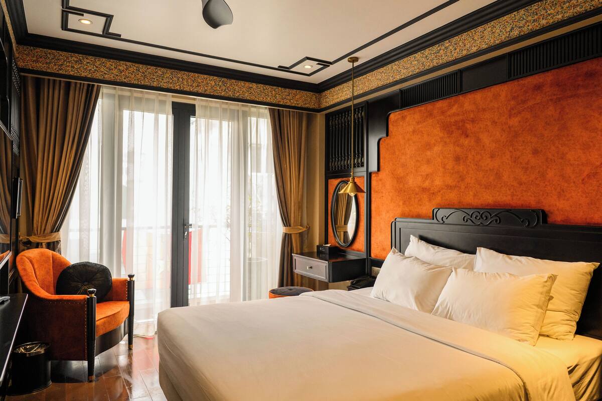 Ein Hotelzimmer mit einem großen Bett, einem Sessel, einem Schreibtisch und einem Fenster mit Vorhängen.