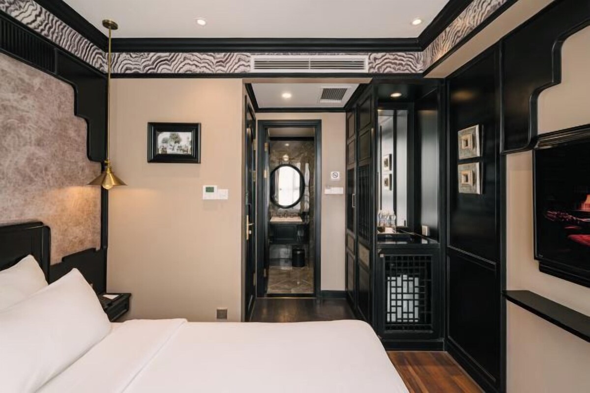 A hotel room with a bed, a nightstand, a lamp, a mirror, and a television.