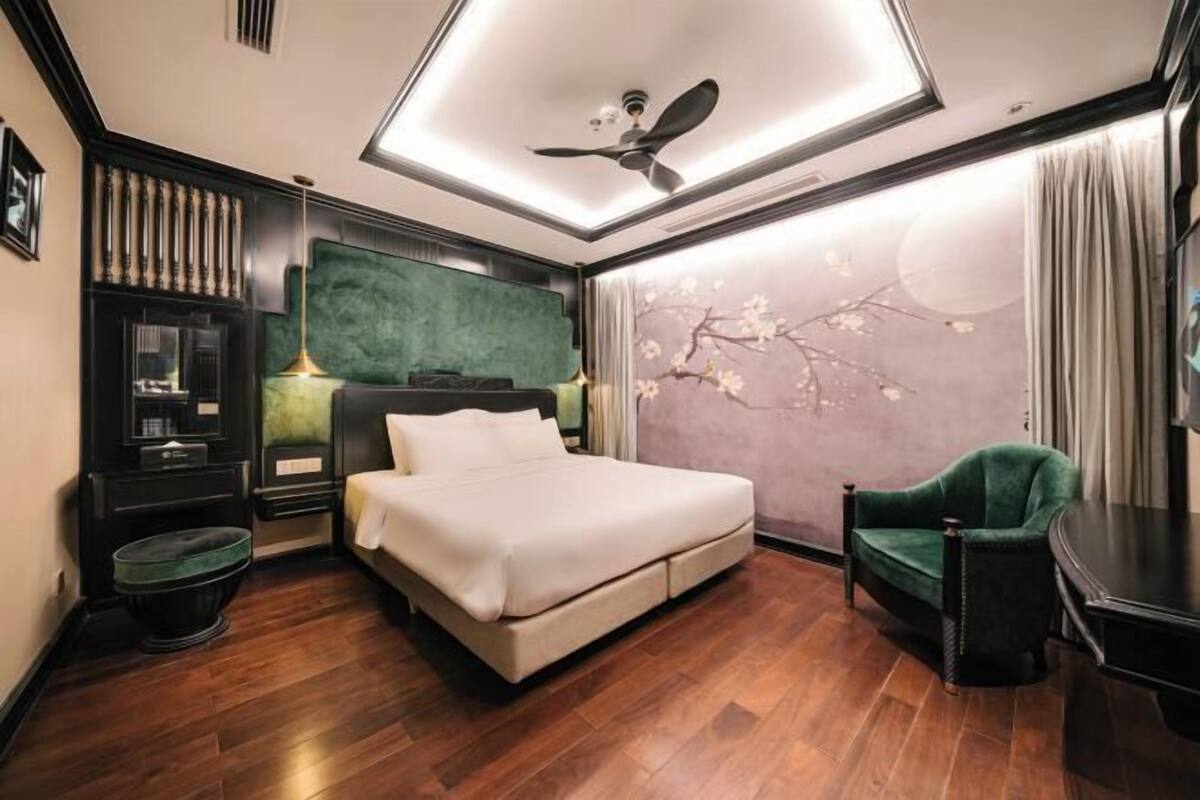 Ein modernes Schlafzimmer mit einem Bett, einem grünen Sessel, einem Deckenventilator und einer Wanddekoration.
