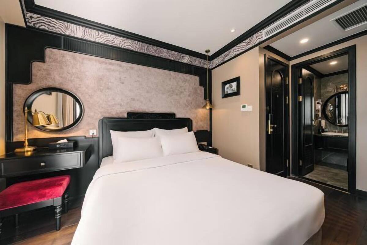 Ein Hotelzimmer mit einem großen Bett, einem Schreibtisch mit Stuhl, einem Spiegel und einer roten Bank.