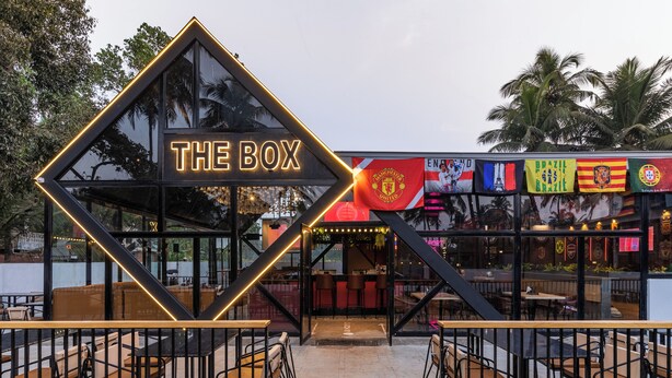 A modern restaurant named "The Box" with a distinctive geometric entrance, outdoor seating, and various national flags displayed. - The Upper House By Mystical Views (Morjim)
