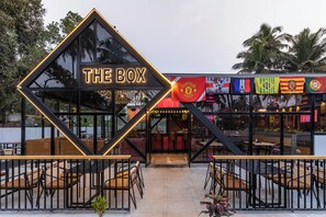 A modern restaurant named "The Box" with a distinctive geometric entrance, outdoor seating, and various national flags displayed. - The Upper House By Mystical Views (Morjim)