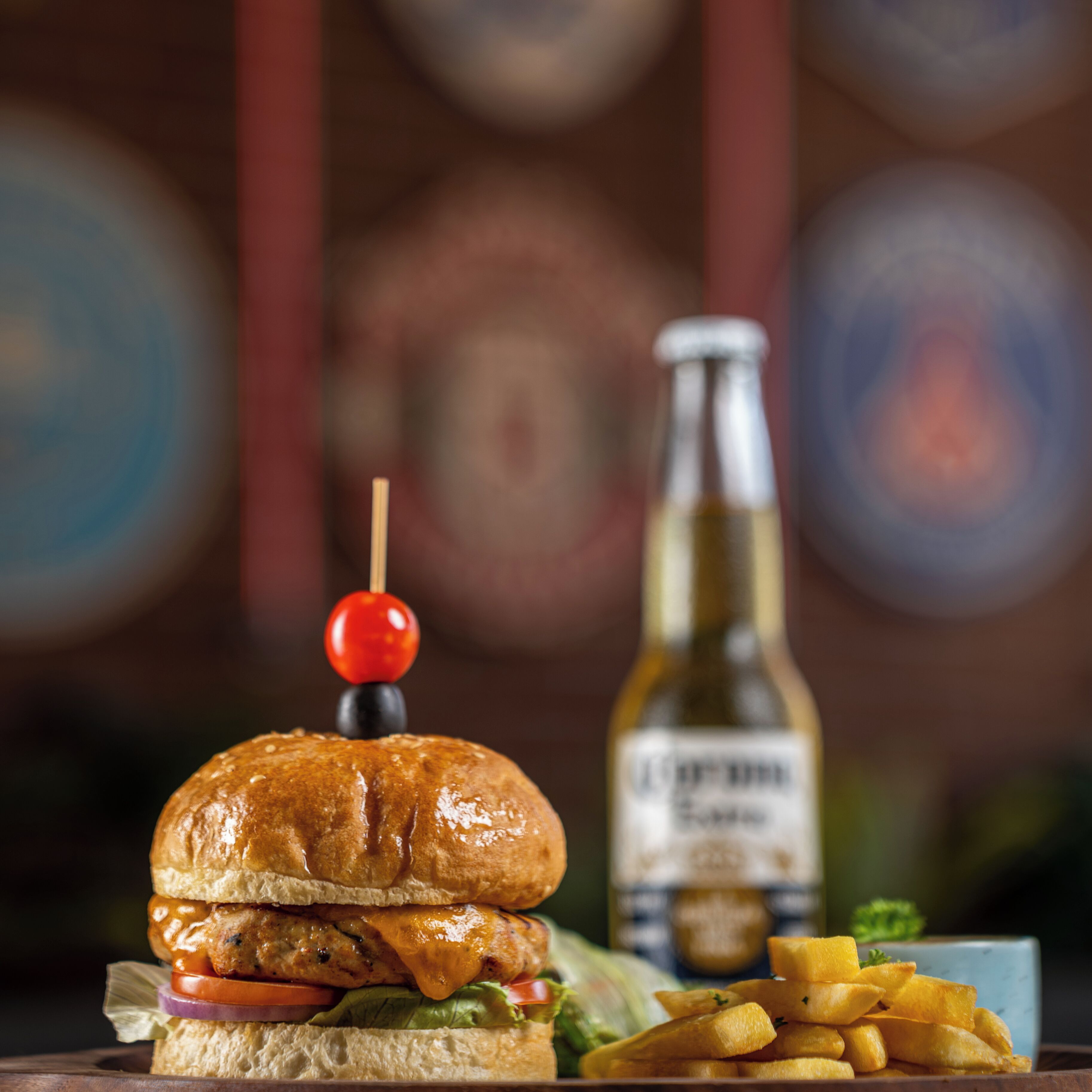A burger with a skewer, a bottle of beer, and fries on a wooden table.